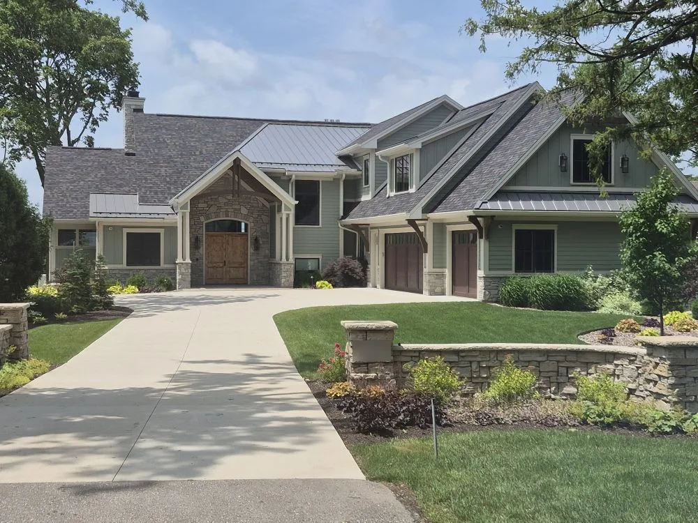Craftsman home with sage siding, stone entry, shingle roof and standing-seam metal accents